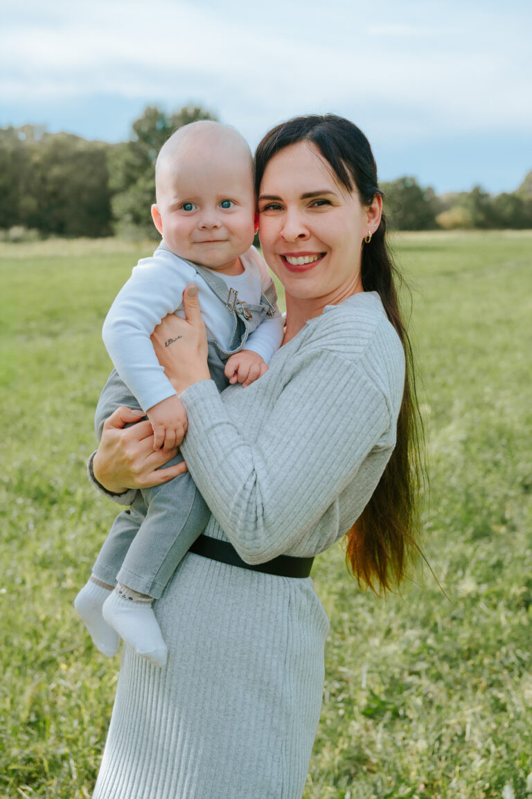 Maminka drží usměvavé miminko v náručí při rodinném focení v přírodě