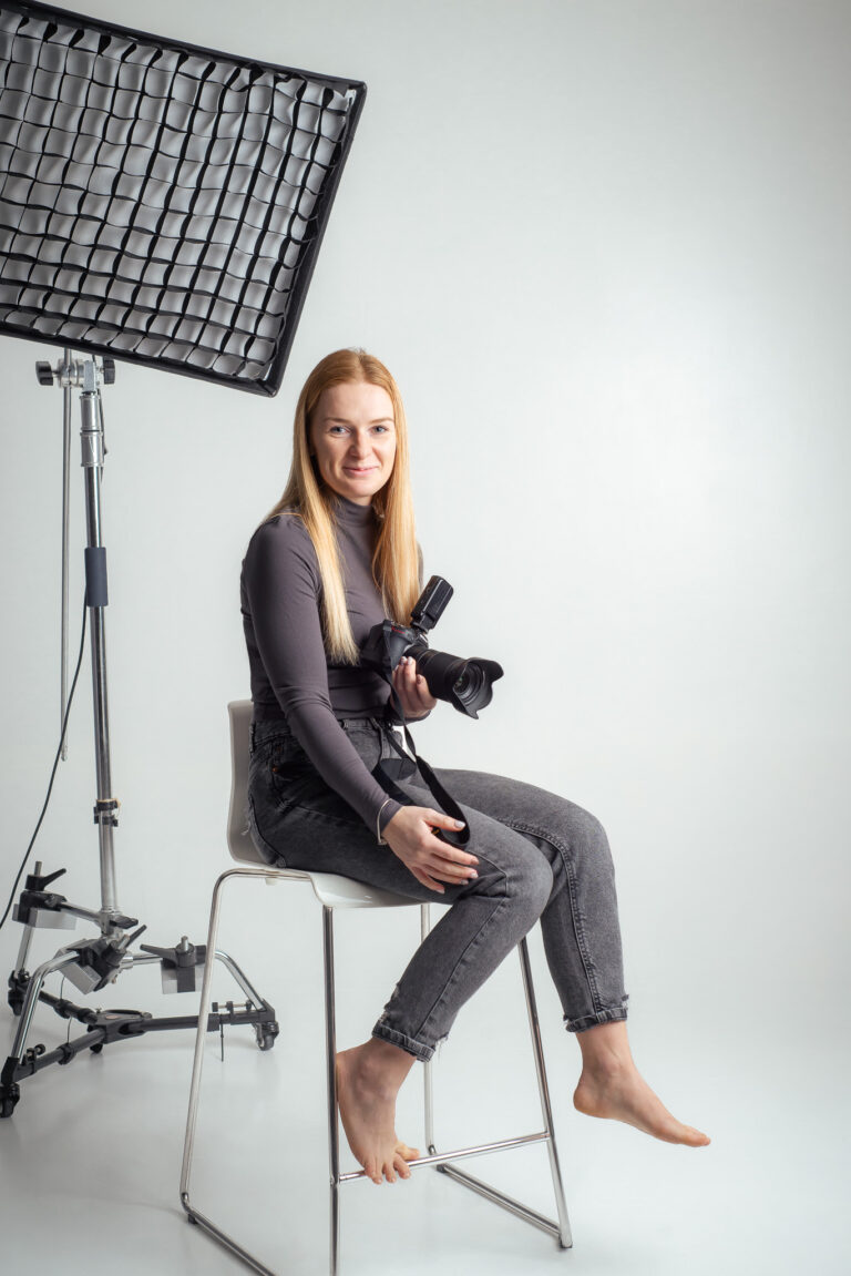Blondýna fotografka s foťákem sedící na vysoké židli držící fotoaparát