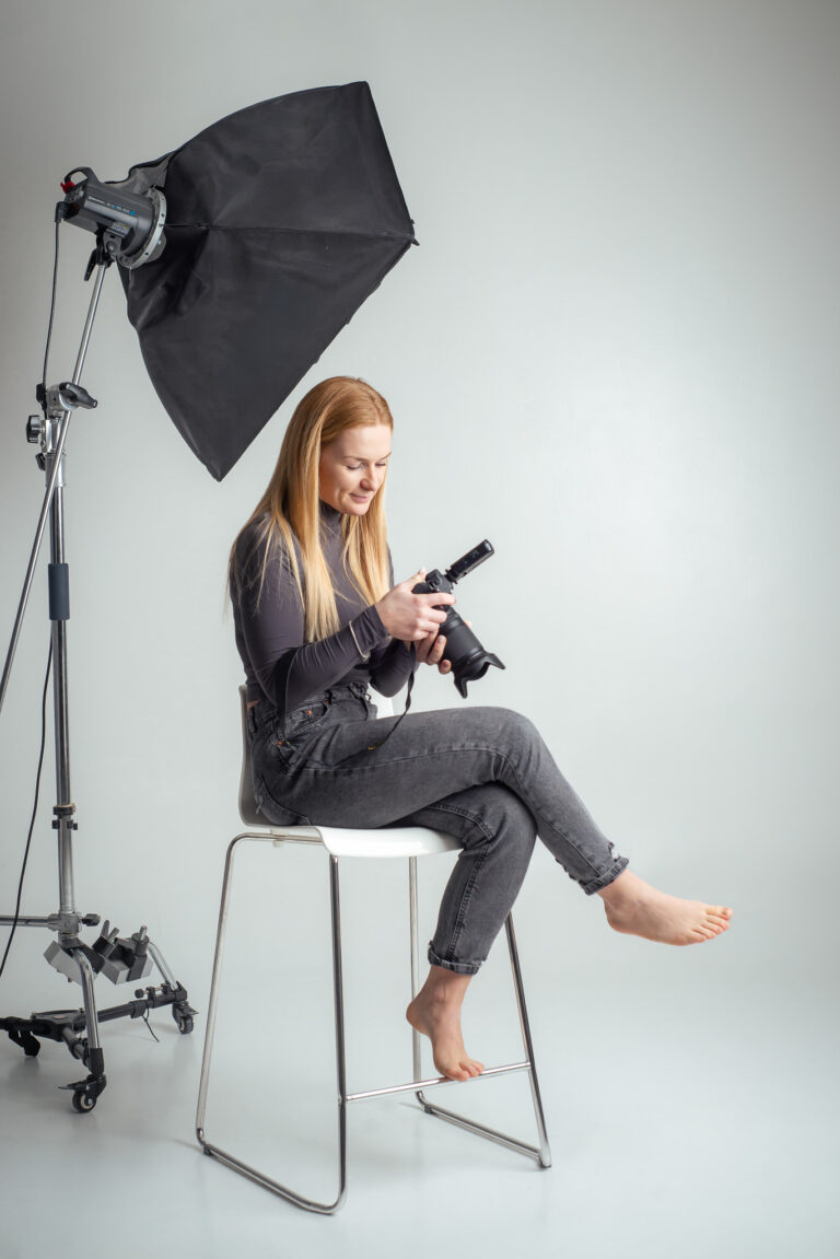 Blondýna fotografka s foťákem sedící na vysoké židli držící fotoaparát