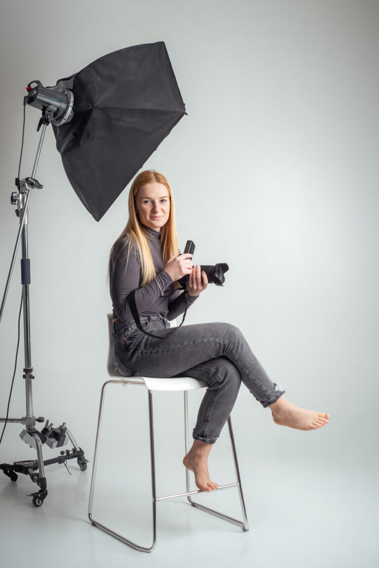 Blondýna fotografka s foťákem sedící na vysoké židli držící fotoaparát
