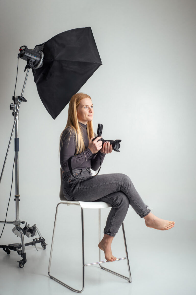 Blondýna fotografka s foťákem sedící na vysoké židli držící fotoaparát