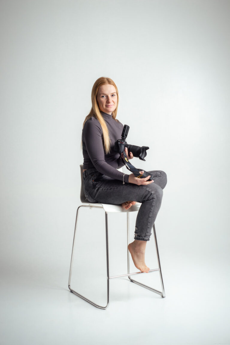 Blondýna fotografka s foťákem sedící na vysoké židli držící fotoaparát