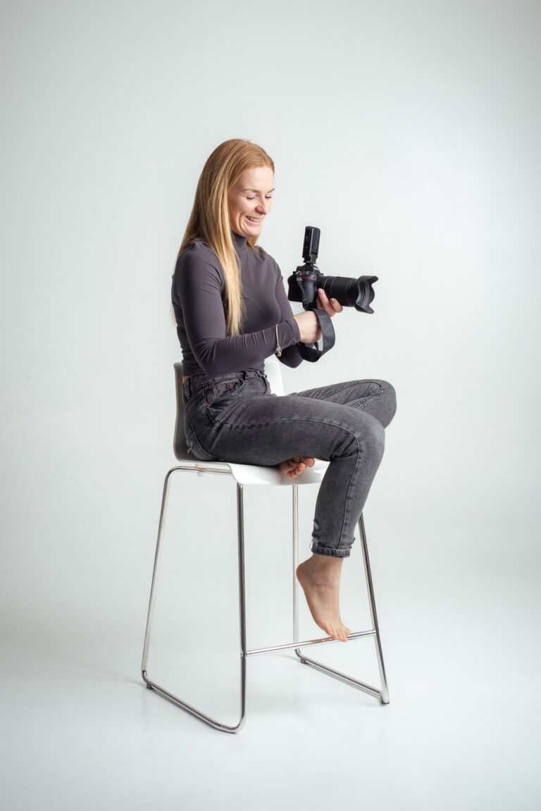 Blondýna fotografka s foťákem sedící na vysoké židli držící fotoaparát