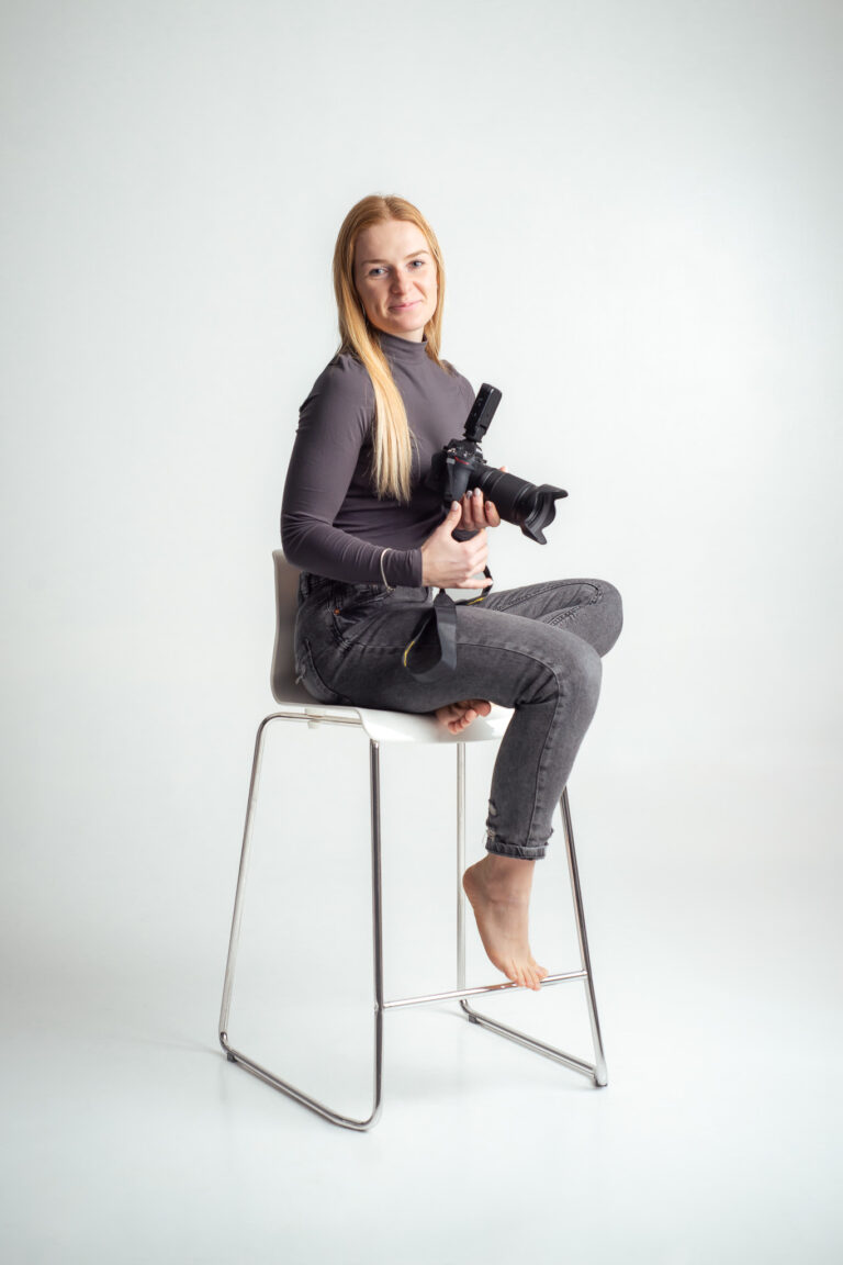 Blondýna fotografka s foťákem sedící na vysoké židli držící fotoaparát