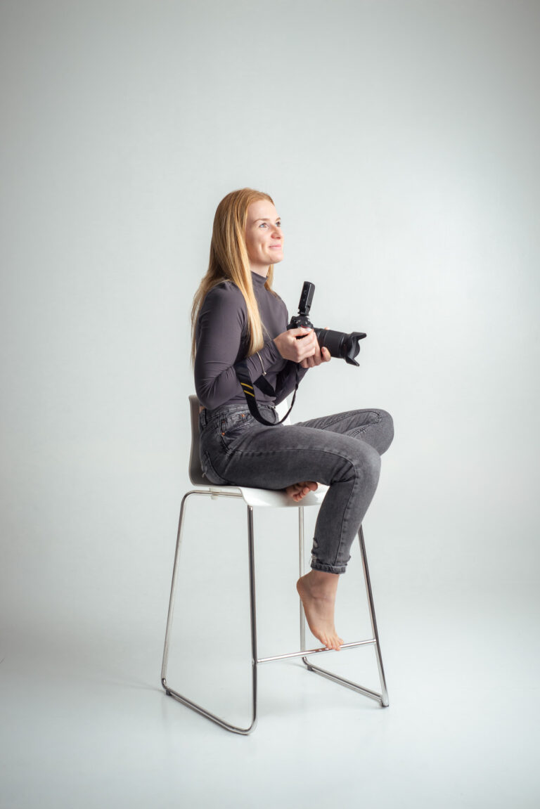 Blondýna fotografka s foťákem sedící na vysoké židli držící fotoaparát