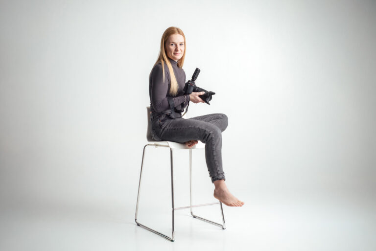 Blondýna fotografka s foťákem sedící na vysoké židli držící fotoaparát