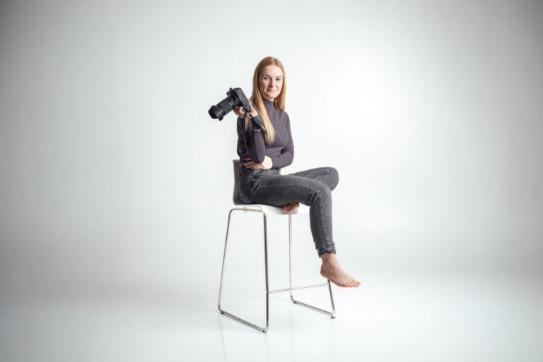 Blondýna fotografka s foťákem sedící na vysoké židli držící fotoaparát