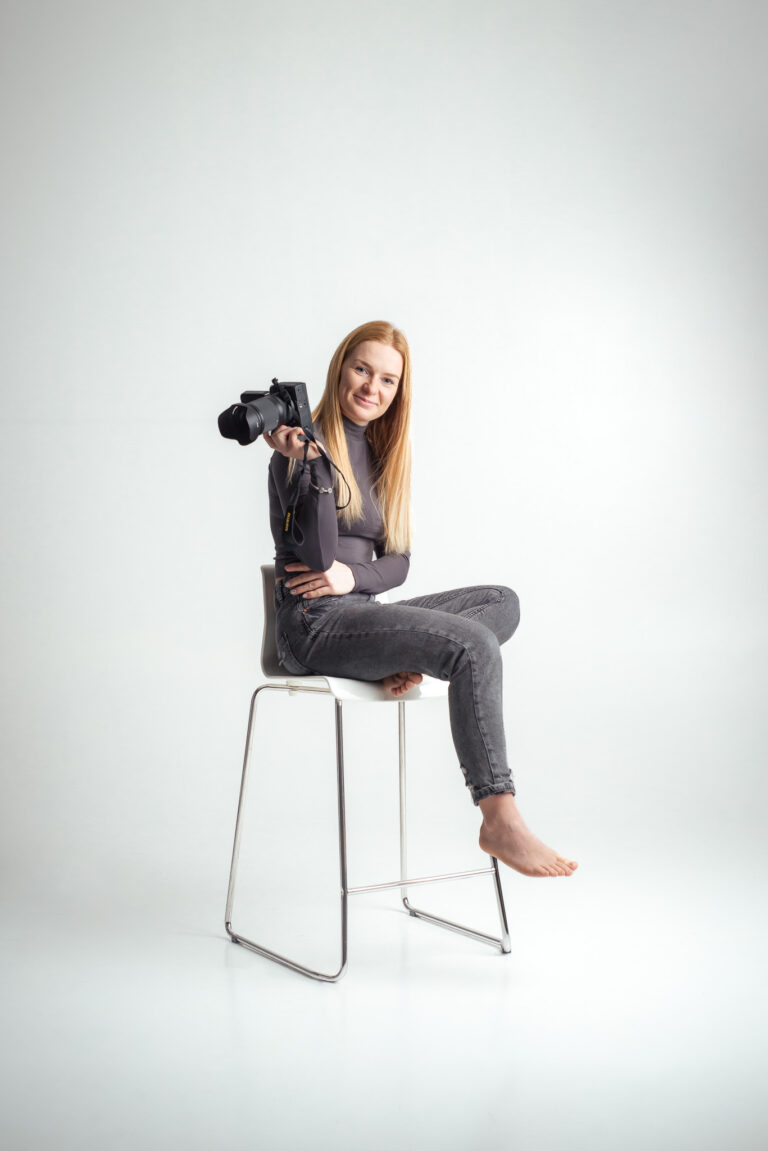 Blondýna fotografka s foťákem sedící na vysoké židli držící fotoaparát