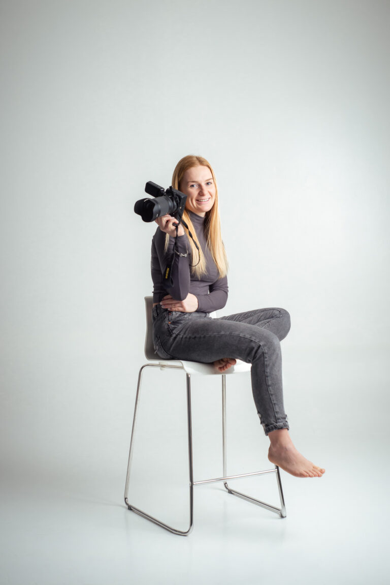 Blondýna fotografka s foťákem sedící na vysoké židli držící fotoaparát