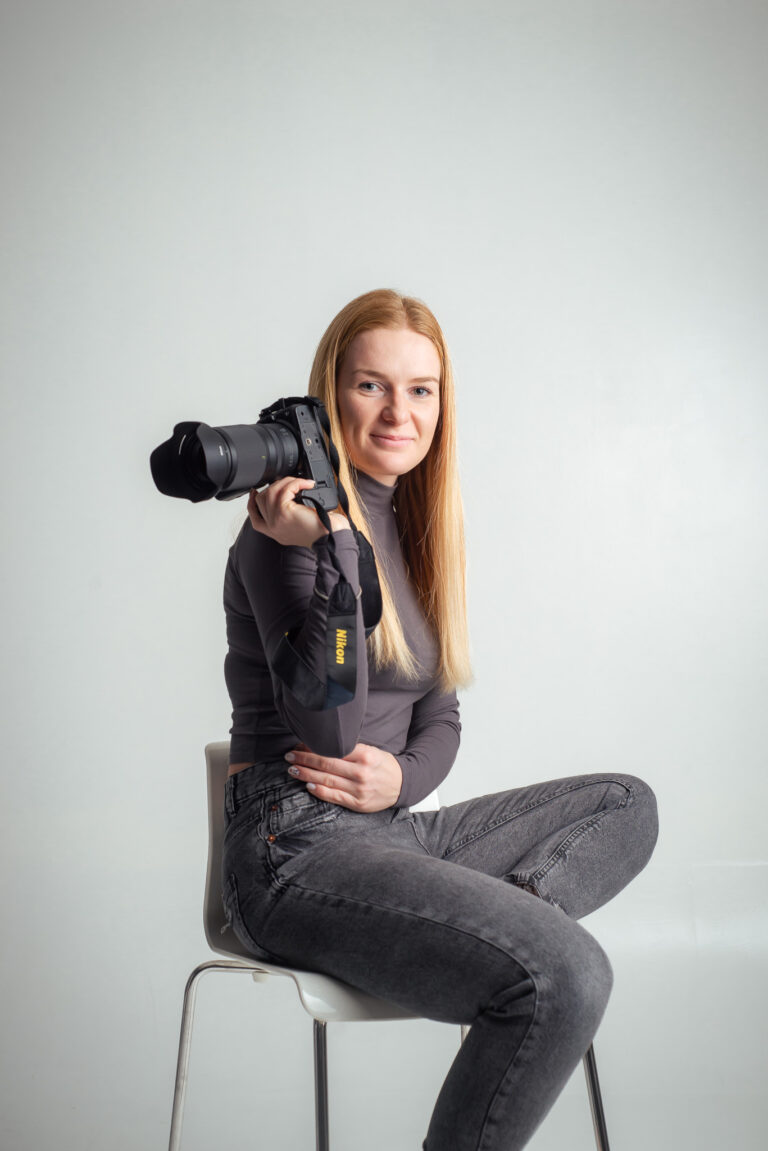 Blondýna fotografka s foťákem sedící na vysoké židli držící fotoaparát
