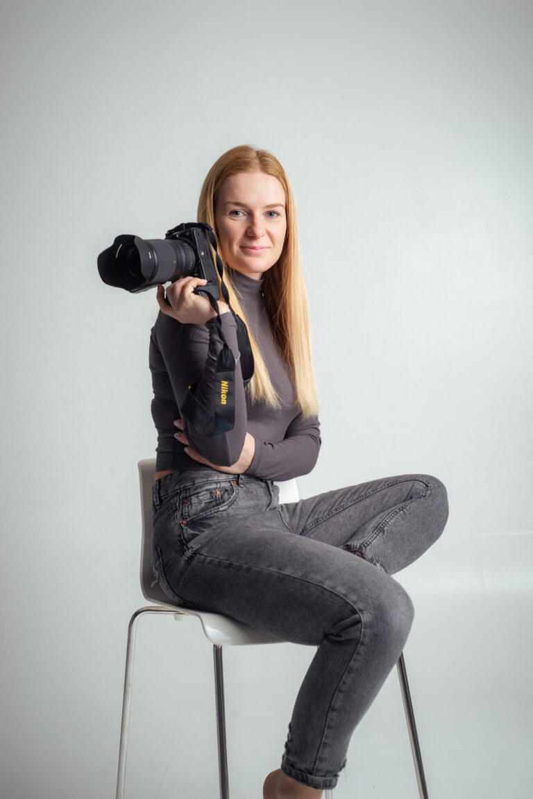 Blondýna fotografka s foťákem sedící na vysoké židli držící fotoaparát