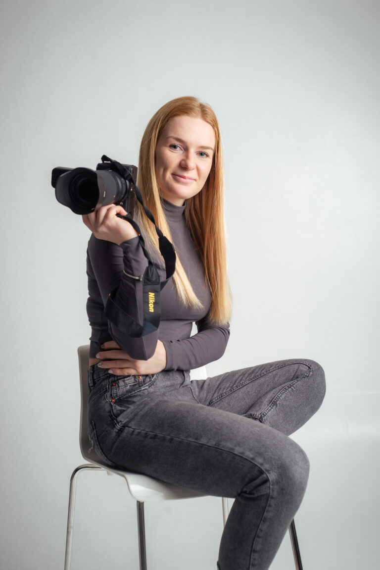 Blondýna fotografka s foťákem sedící na vysoké židli držící fotoaparát