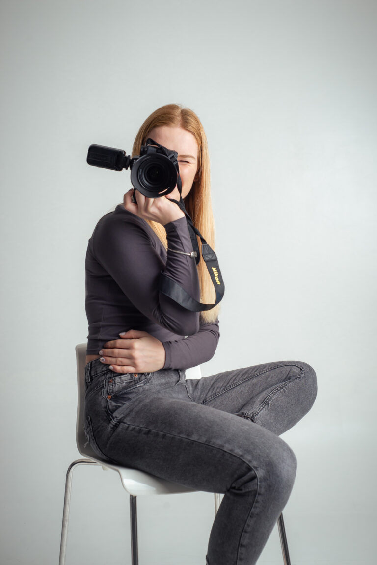 Blondýna fotografka s foťákem sedící na vysoké židli držící fotoaparát
