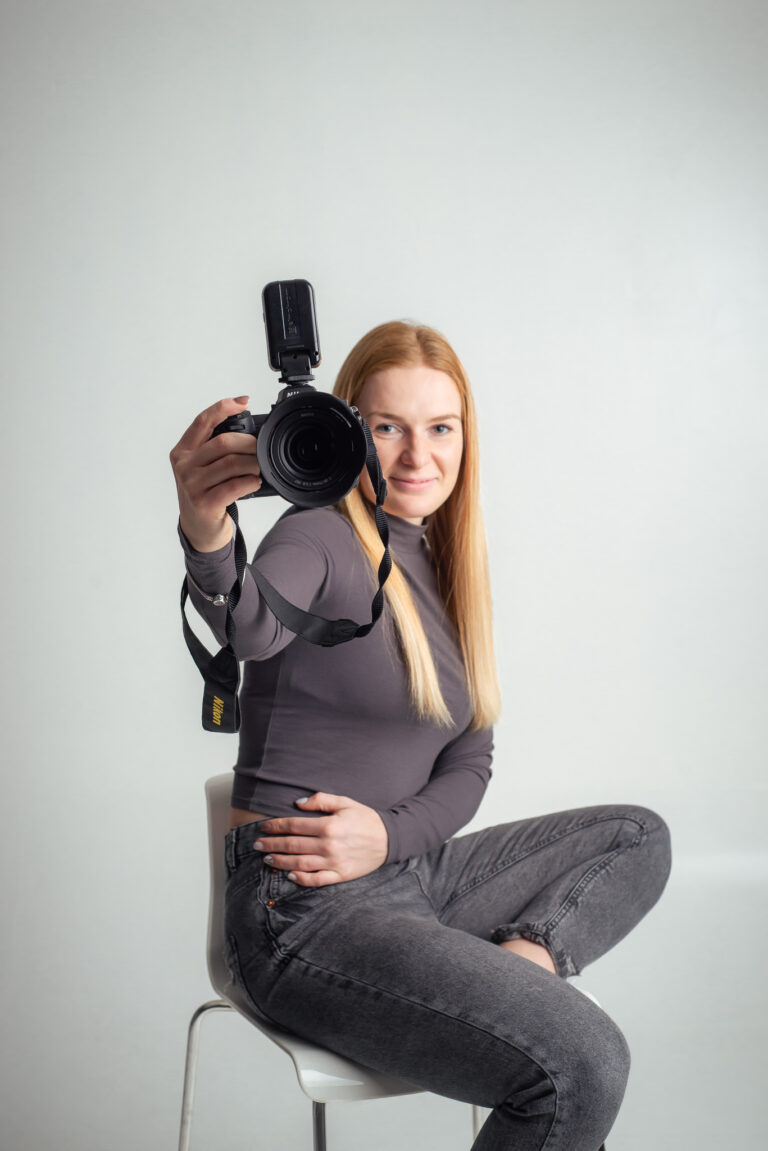 Blondýna fotografka s foťákem sedící na vysoké židli držící fotoaparát