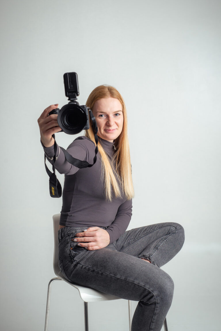 Blondýna fotografka s foťákem sedící na vysoké židli držící fotoaparát