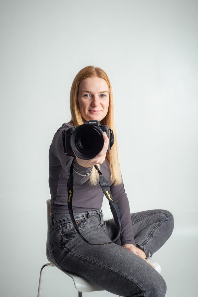 Blondýna fotografka s foťákem sedící na vysoké židli držící fotoaparát
