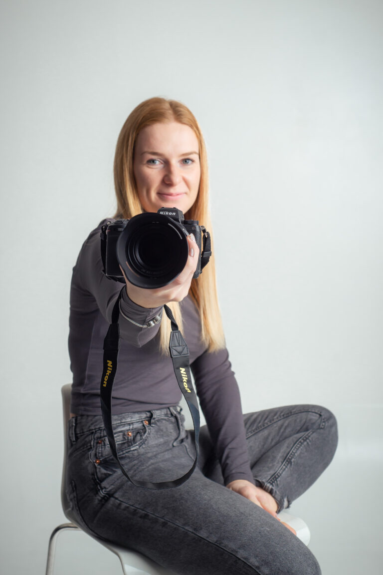 Blondýna fotografka s foťákem sedící na vysoké židli držící fotoaparát