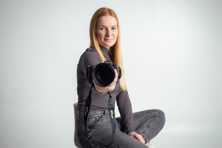 Blondýna fotografka s foťákem sedící na vysoké židli držící fotoaparát