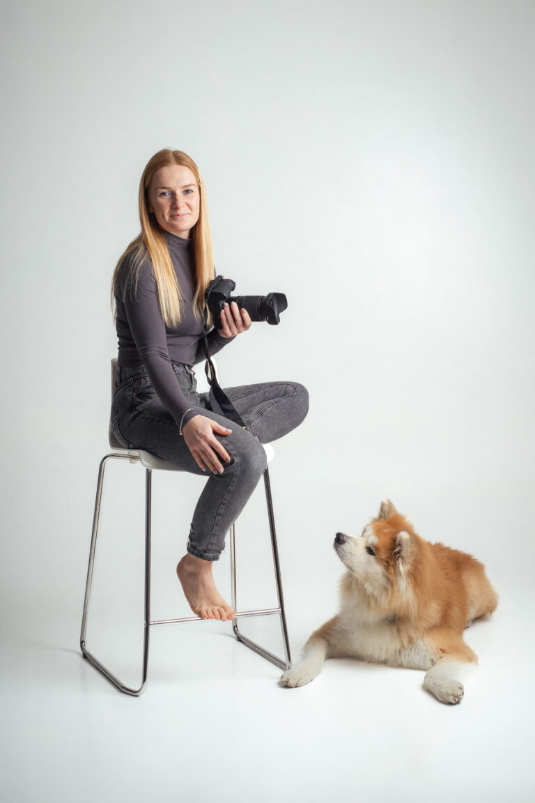 Blondýna fotografka s foťákem sedící na vysoké židli držící fotoaparát se psem