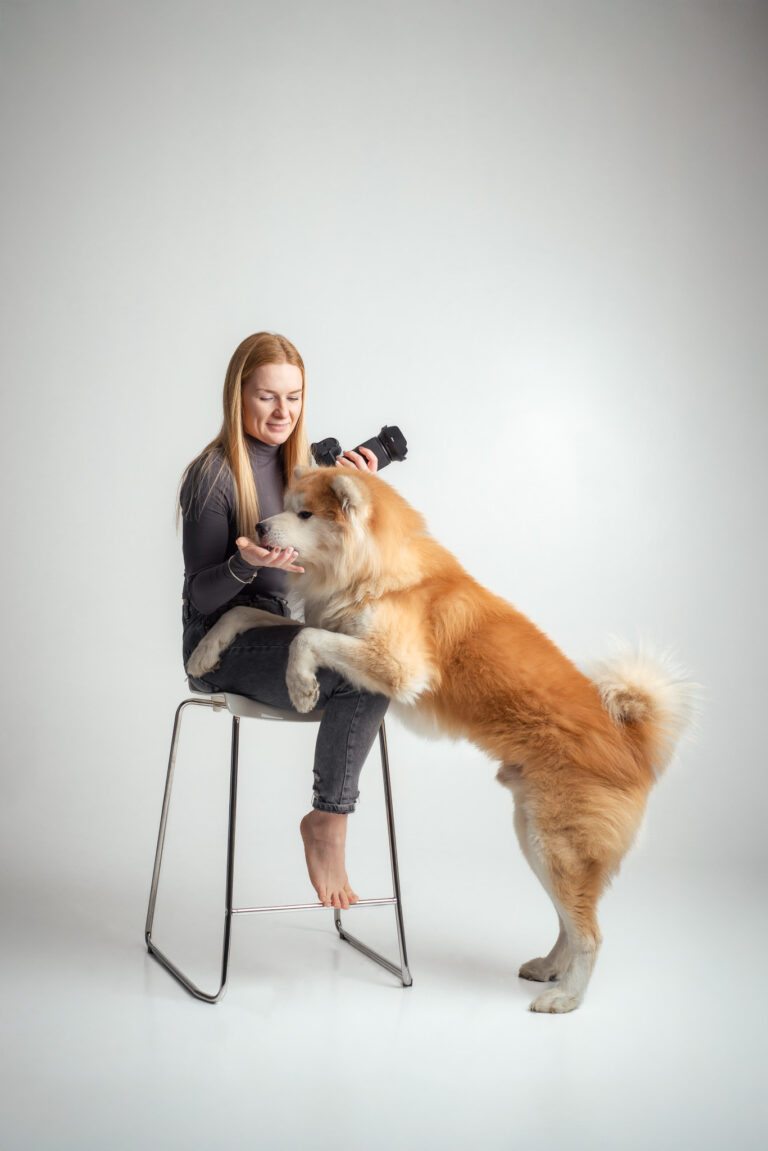 Blondýna fotografka s foťákem sedící na vysoké židli držící fotoaparát se psem