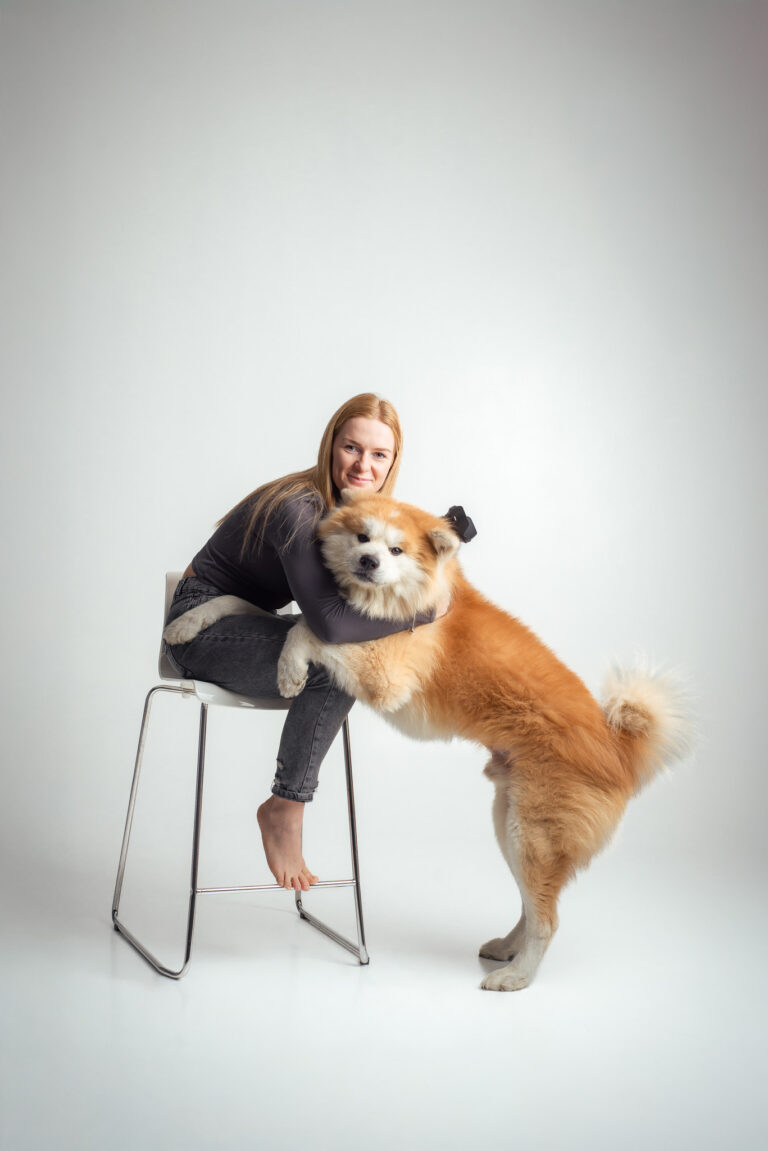 Blondýna fotografka s foťákem sedící na vysoké židli držící fotoaparát se psem