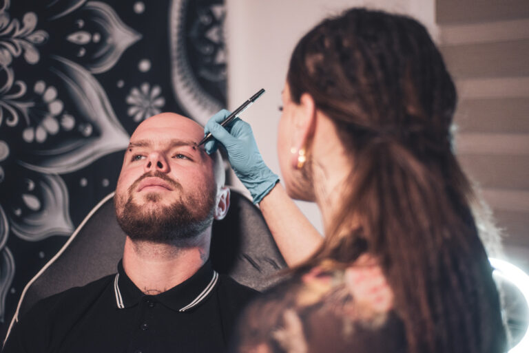 Potetovaná holka s dredama dělající piercing holohlavému muži na obočí