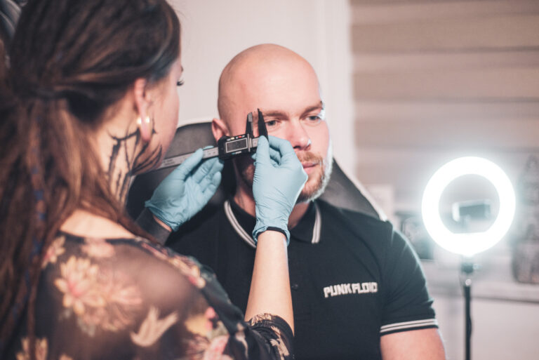 Potetovaná holka s dredama dělající piercing holohlavému muži na obočí