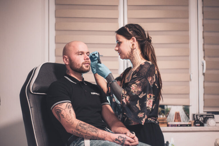 Potetovaná holka s dredama dělající piercing holohlavému muži na obočí
