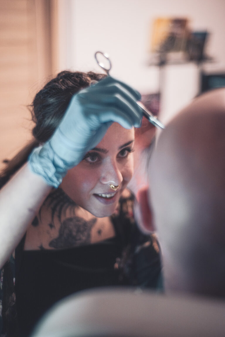 Potetovaná holka s dredama dělající piercing holohlavému muži na obočí