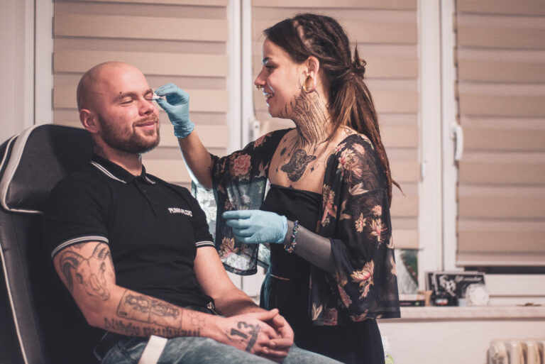 Potetovaná holka s dredama dělající piercing holohlavému muži na obočí