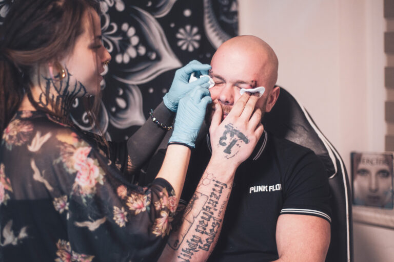 Potetovaná holka s dredama dělající piercing holohlavému muži na obočí