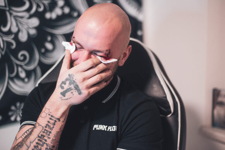 Potetovaná holka s dredama dělající piercing holohlavému muži na obočí